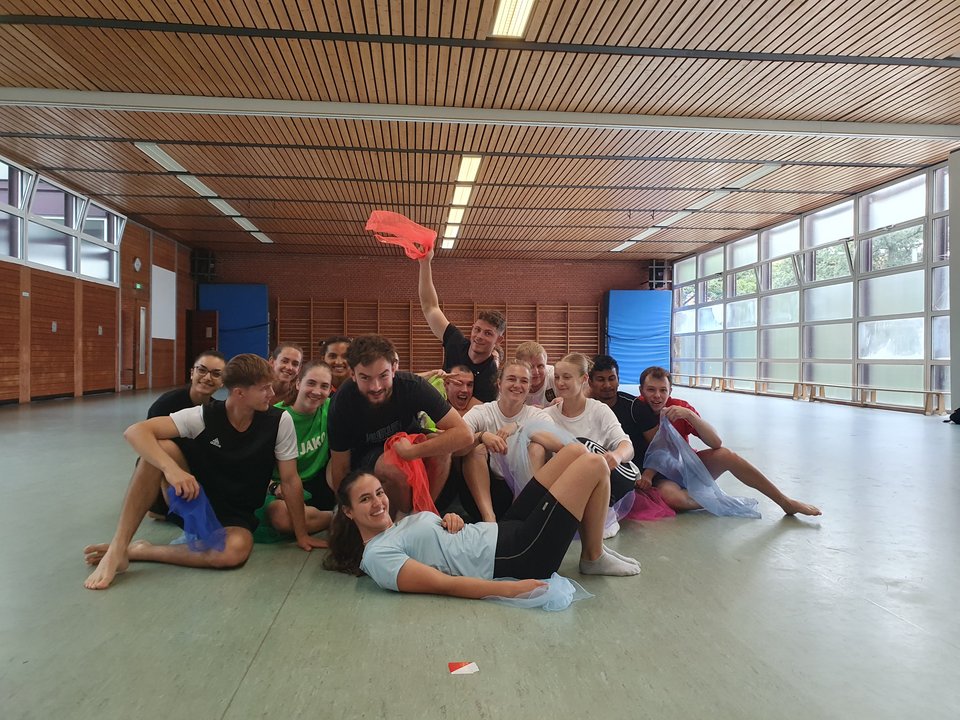 Eine Gruppe Studierender posiert fröhlich in einer Sporthalle