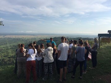 Das Bild zeigt die praktische Arbeit im Feld der Geographie. Zusehen ist eine Gruppe von Studierenden, die die umliegende Landschaft betrachten und einzelne Besonderheiten vom Dozenten im Feld durch Zeigen und Erklärungen erläutert bekommen.