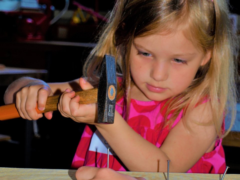 Ein Kindergartenkind schlägt mit einem Hammer einen Nagel ein