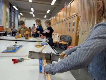 Ein Mädchen arbeitet mit einer Säge an einem Werktisch