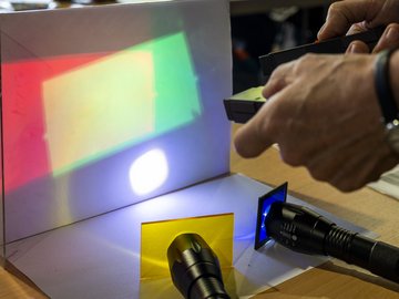 Ein Versuchsaufbau mit Glasplättchen in verschiedenen Farben und Taschenlampen, die von hinten gegen diese leuchten.