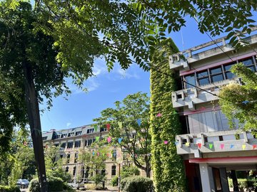 Blick über den grünen Innenhof auf dem Campus der PHKA. Zwischen zwei Bäumen hängt eine Wimpelkette für ein Fest.