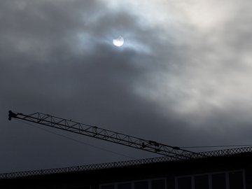 Die Sonne ist hinter Wolken verborgen. Ein Ansatz der Sonnenfinsternis ist zu sehen.