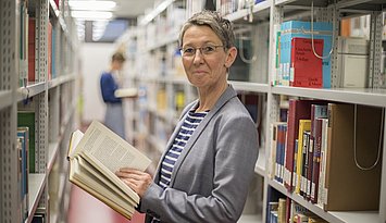 Eine Person steht zwischen Bücherregalen in einer Bibliothek.