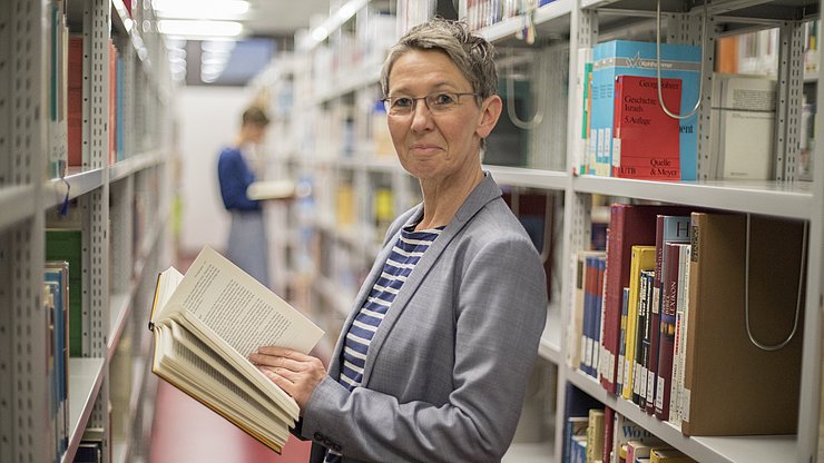 Eine Person steht zwischen Bücherregalen in einer Bibliothek.