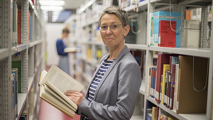Eine Person steht zwischen Bücherregalen in einer Bibliothek.