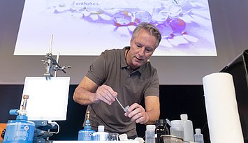 Prof. Ducci beim Experimentieren mit Pipette, Becherglas, Chemikalien und Bunsenbrenner. 