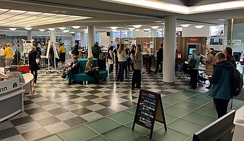 Im Foyer der Stadtbibliothek Karlsruhe treffen TeilnehmerInnen zum Fachtag für Lesepat:innen und Lehrkräfte ein. Es sind Personen im Gespräch zu sehen.