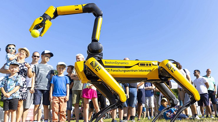 EFFEKTE-Reihe-2024-25_Januar Ein wie ein Vierbeiner anmutender Roboter nimmt auf einer Wiese Bälle auf, im Hintergrund staundende Kinder und Erwachsene