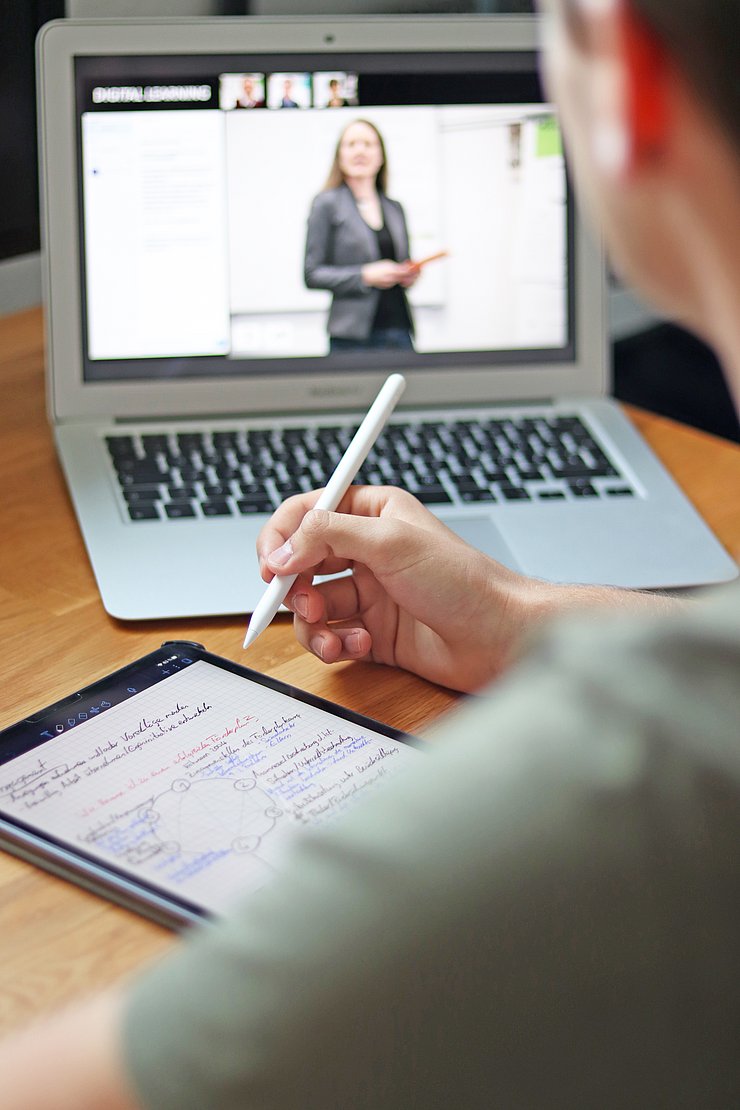 Eine Person, von hinten fotografiert, arbeitet mit Touch Pen und Laptop.