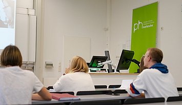 Studierende von hinten in einem mit moderner Medientechnik ausgestatteten Hörsaal