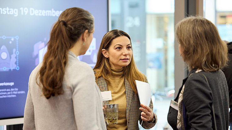 EFFEKTE-Reihe-2024-25-Februar Drrei Frauen unterhalten sich vor einem wissenschaftlichen Poster