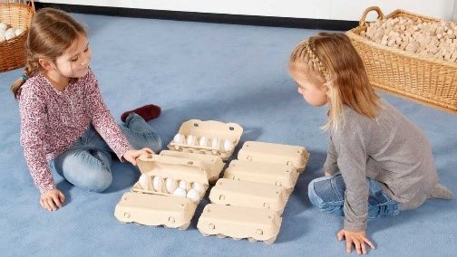 Zwei kleine Mädchen sortieren Eier in Eierschachteln. Beispiel für das Erkennen von Zahlzerlegungen auf enaktiver Ebene