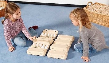 Zwei kleine Mädchen sortieren Eier in Eierschachteln. Beispiel für das Erkennen von Zahlzerlegungen auf enaktiver Ebene